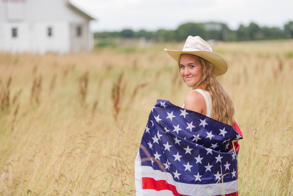 Waynedale senior girl holding American flag standing in wheat field. Photographed by Jamie Lynette Photography, Wayne County Senior Portrait Photographer. 