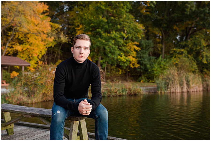sippo lake fall senior session, perry high school student sitting on bench by water with beautiful fall leaves behind. 