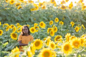 high school senior student is standing in a field of sunflowers with a serious face, senior is standing in far left of photo, using the rule of thirds.