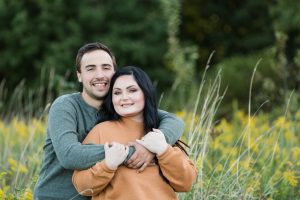 engaged couple, standing in tall grass with flowers behind