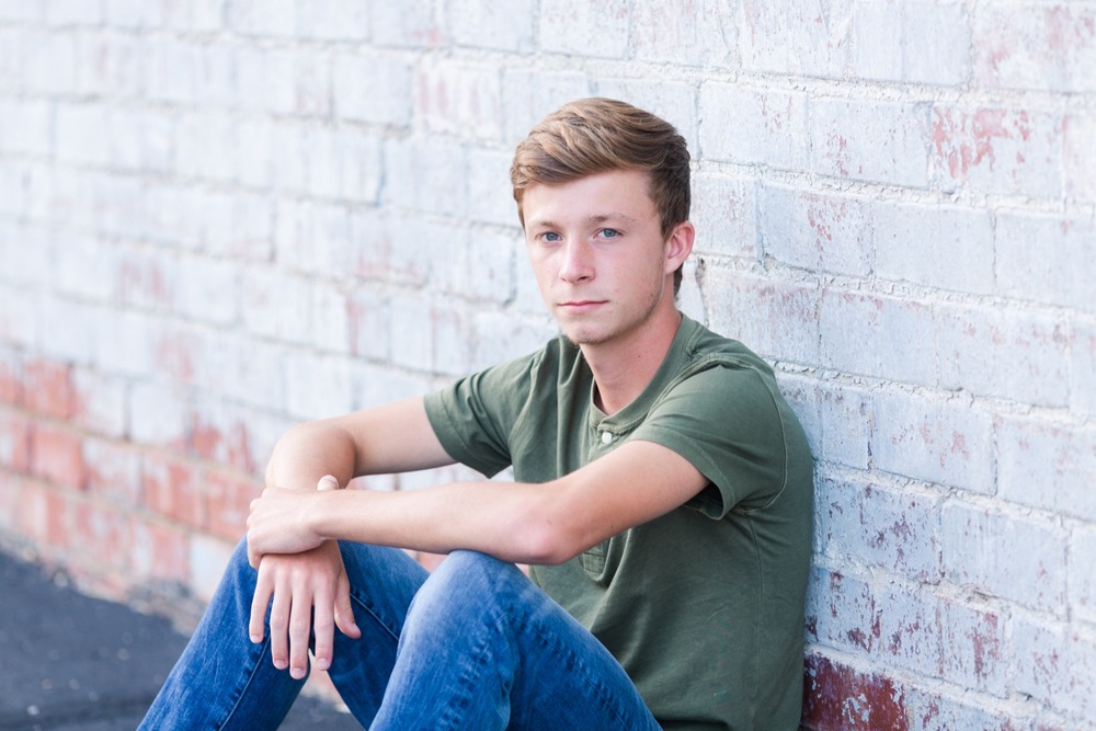Senior guy leaning against brick wall