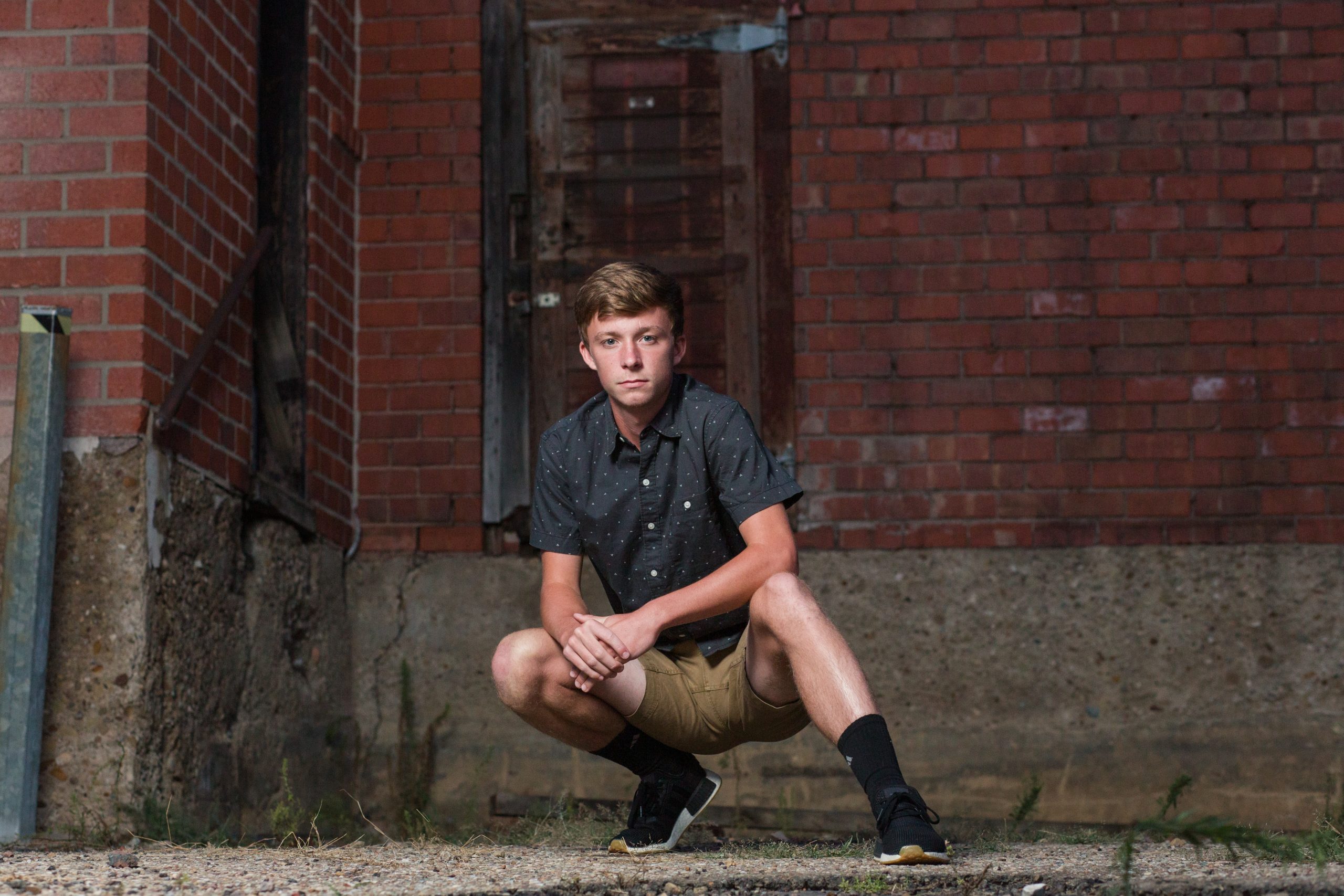 senior guy crouched down in front of a rustic old building