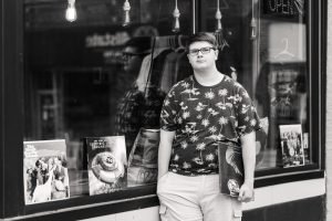 black and white photo of high school senior guy standing outside of a record store