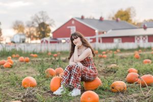 high school senior sitting on pumpkin in pumpkin patch
