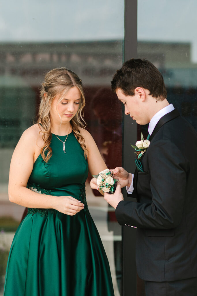 Prom couple putting flowers on each other in Wooster, Ohio, captured by Jamie Lynette Photography. The girl is wearing a green dress and the boy is in a black tux, sharing a joyful moment before prom. These are from their Prom Mini Session.
