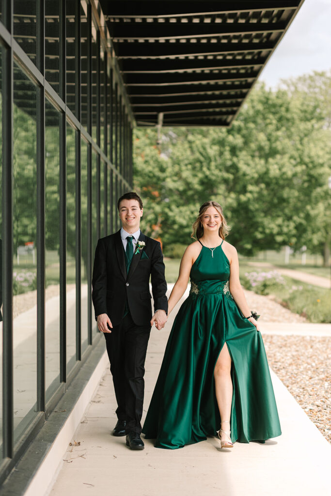 Prom couple walking in Wooster, Ohio, captured by Jamie Lynette Photography. The girl is wearing a green dress and the boy is in a black tux, sharing a joyful moment before prom. These are from their Prom Mini Session.
