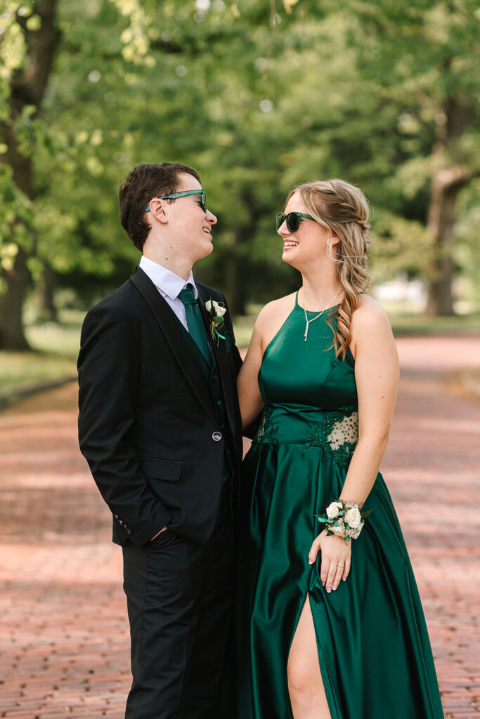 Prom couple with sunglasses on being silly in Wooster, Ohio, captured by Jamie Lynette Photography. The girl is wearing a green dress and the boy is in a black tux, sharing a joyful moment before prom. These are from their Prom Mini Session.