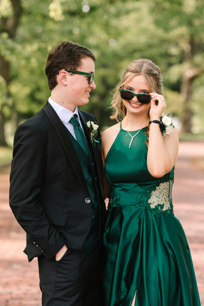 Prom couple with sunglasses on being silly in Wooster, Ohio, captured by Jamie Lynette Photography. The girl is wearing a green dress and the boy is in a black tux, sharing a joyful moment before prom. These are from their Prom Mini Session.